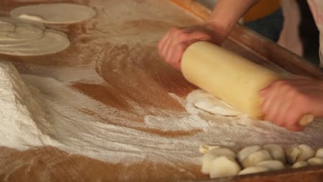 cook sprinkling flour and rolling thin dough with roller pin at kitchen table. woman cooking pie dough on home kitchen. preparing italian pizza in restaurant. cooking handmade food concept