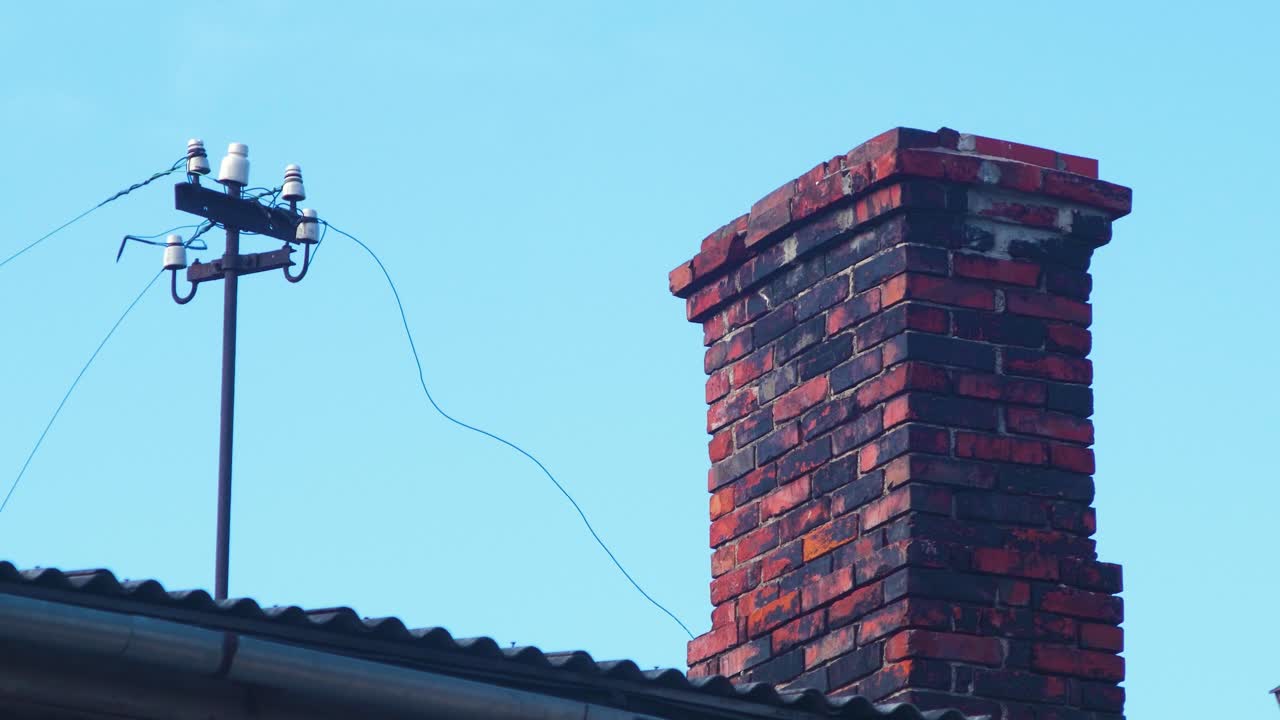 vista de la azotea de la casa antigua con chimenea de ladrillos de arcilla, poste eléctrico antiguo con cables colgantes, techo cubierto con tejas de arcilla roja, día soleado de verano, tiro medio distante