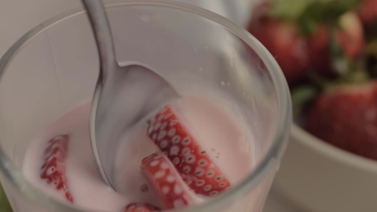 Un cucchiaio mescola da vicino un milkshake fresco con fragole fresche a fette