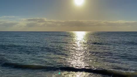 incline lentamente hacia arriba desde las suaves olas de una playa tropical desierta al atardecer hacia el claro horizonte mientras el sol desciende y el cielo se vuelve amarillo