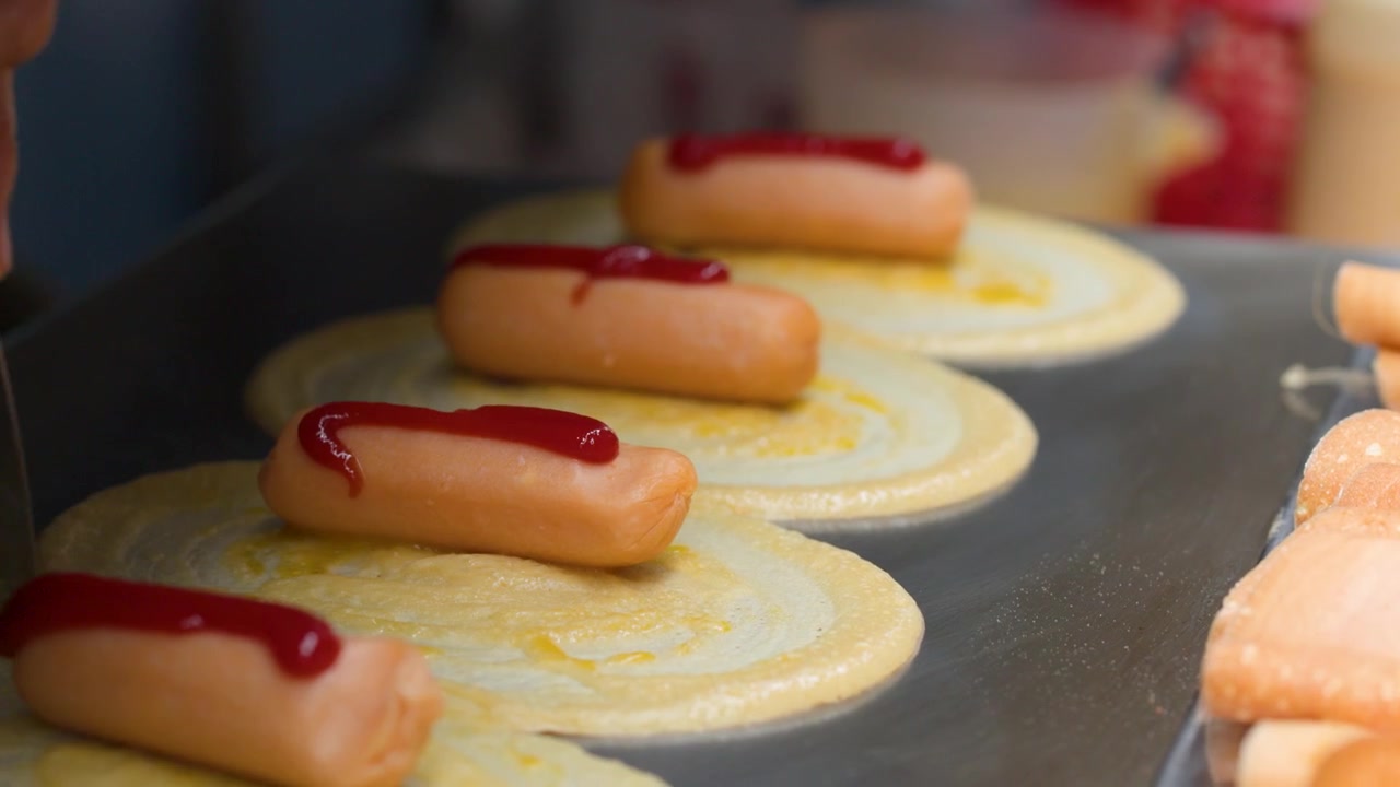 Primo piano di un venditore che usa una spatola per cucinare pancake salati con salsicce
