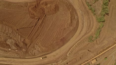 two trucks carrying dirt driving down a curved dusty track on an industrial site