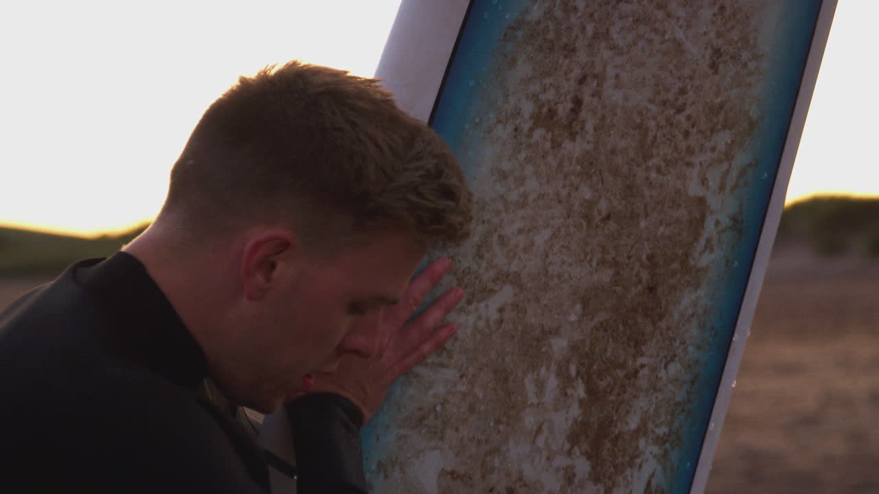 해가 지는 동안 해변에서 서핑 휴가를 즐기는 서핑 보드를 들고 있는 웨이트 슈트를 입은 젊은 남자