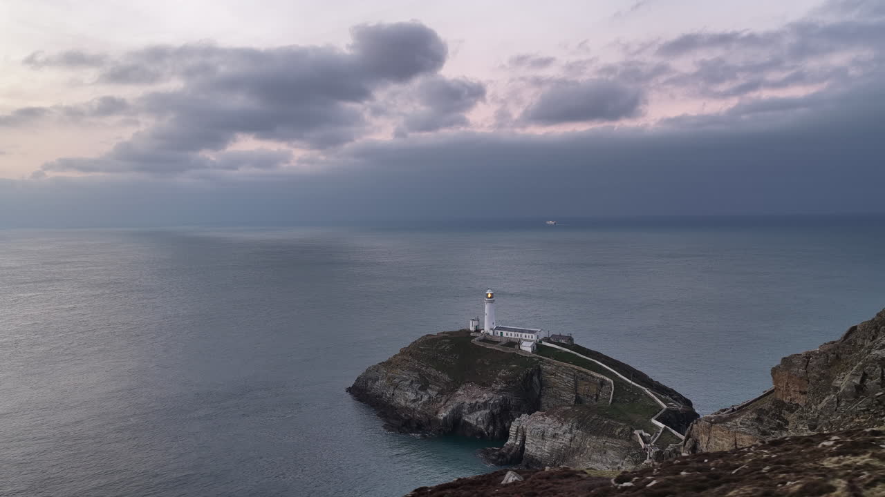 Riprese aeree con drone del Faro di South Stack sulla aspra costa gallese, scogliere drammatiche e onde atlantiche, un paesaggio marino cinematografico ideale per viaggi, natura, turismo costiero e uso documentaristico.