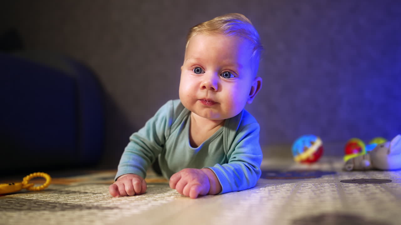 Adorable baby with plump cheeks lies on the floor. Calm kid looking in front of him with interest. Blurred backdrop.