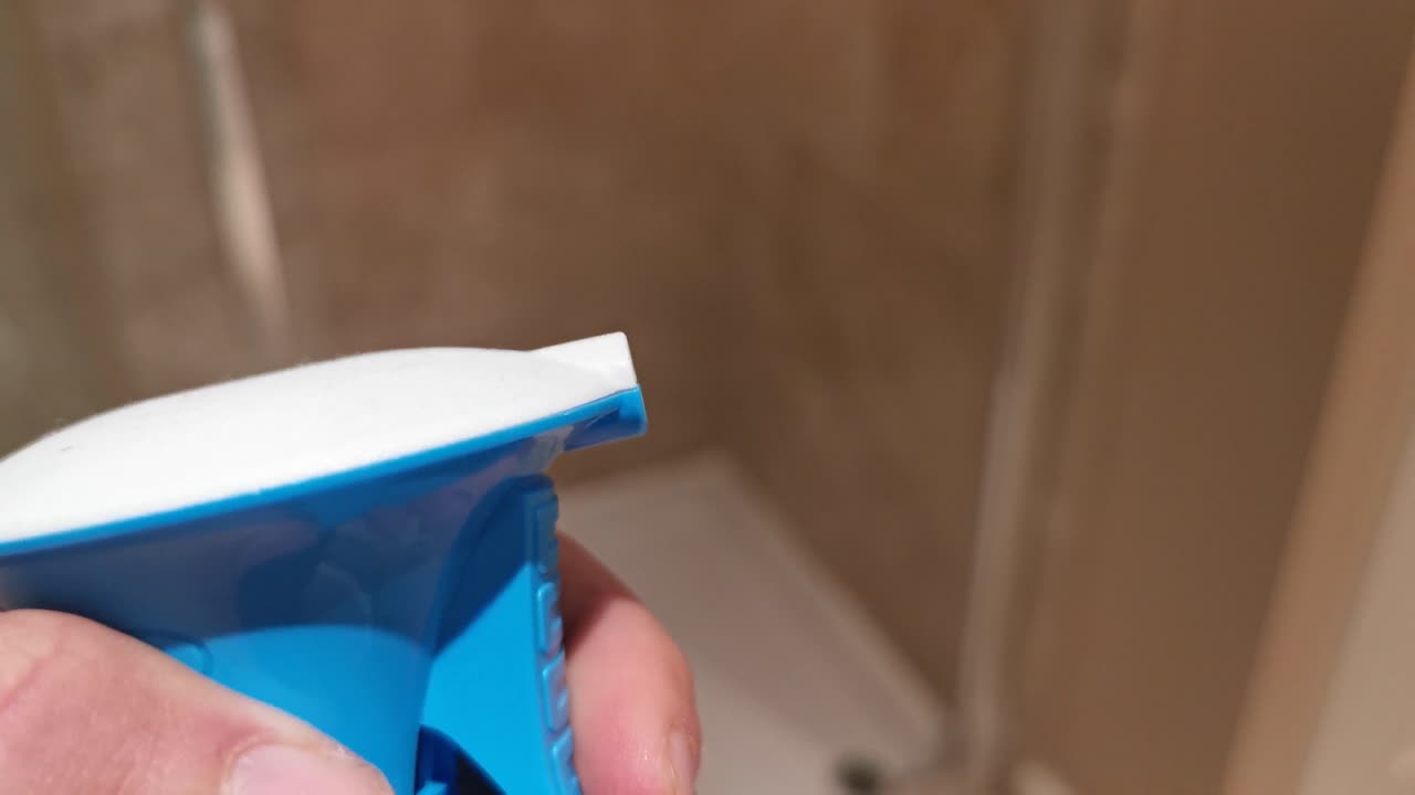 Close-up of a Person's Hand Holding a Blue Spray Bottle in a Bathroom