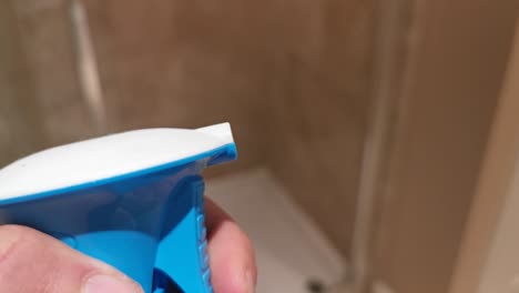 close-up of a person's hand holding a blue spray bottle in a bathroom