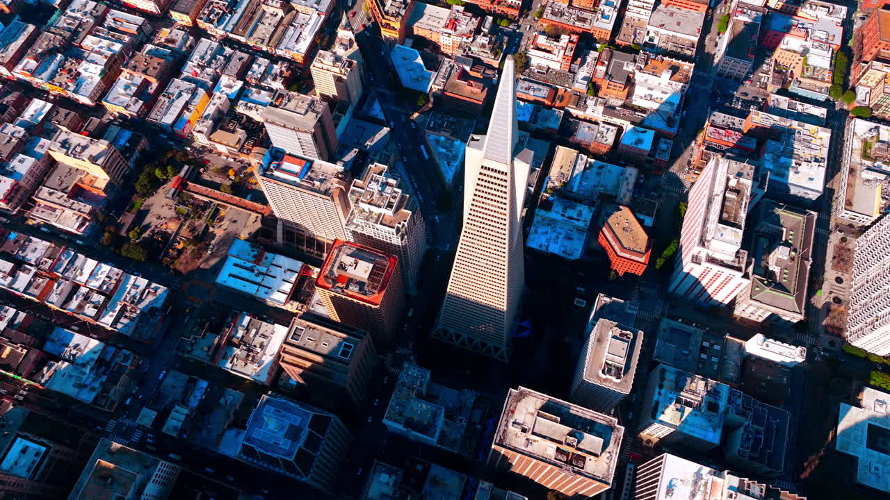 Aerial view above the Transamerica Pyramid building in San Francisco. Surrounding streets, smaller buildings, and rooftops, casting long shadows from the sun