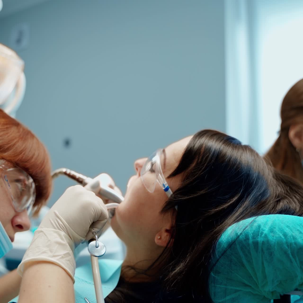 Dental oral procedure in dentistry. Female stomatologist and a nurse in masks treating patient's tooth in modern clinic.