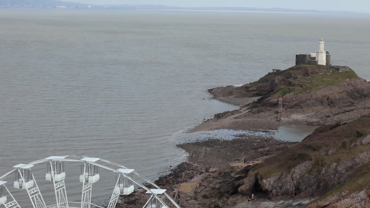 Aerial shot revealing The Big Wheel at Mumbles Pier Swansea with a lighthouse at background in England.