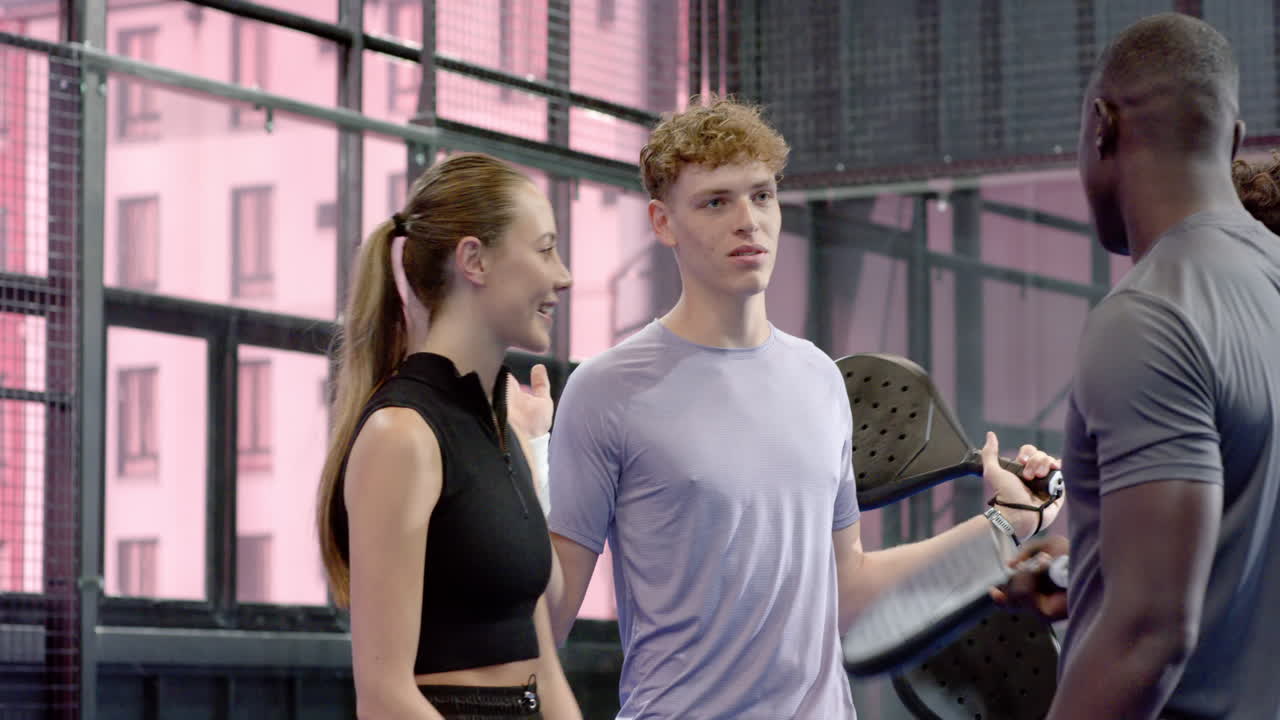 Group of diverse friends enjoying padel tennis on indoor court, smiling and holding rackets