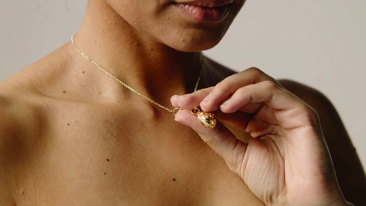 Una donna adulta che porta la mano alla catena, pizzicando e ruotando un piccolo ciondolo d'oro per ispezionarlo in studio.