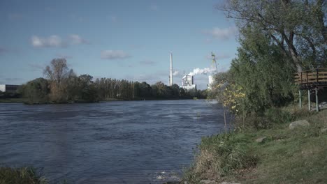 woman in protective suit walking towards camera, river and smoking factory in background, outdoor middle shot view