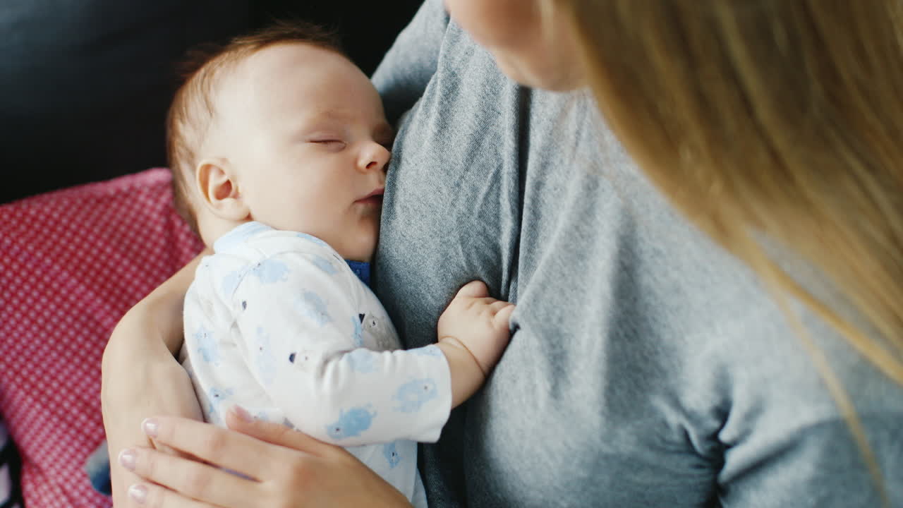 아기는 어깨 너머로 어머니 뒷모습의 품에서 달콤하게 잔다