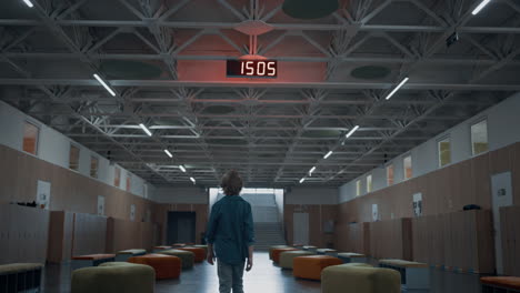 rear view schoolboy walking empty hall. teen boy passing lockers in corridor.