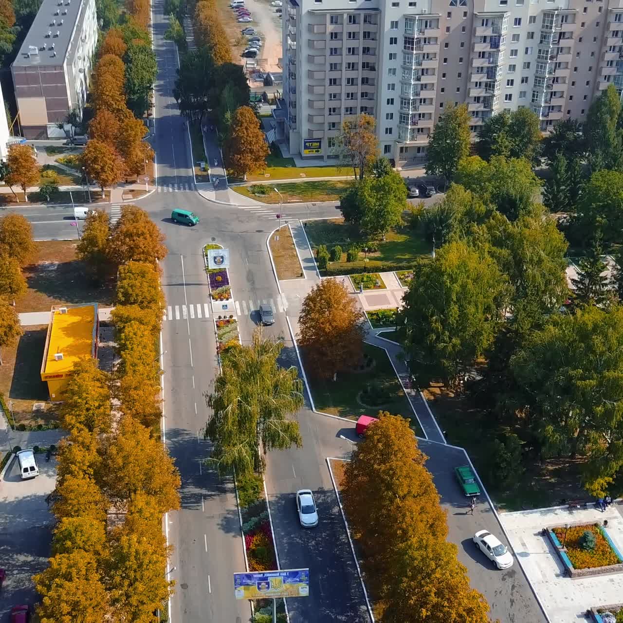 Cars and pedestrians moving by the city streets on sunny day. Residential area with green and orange trees in autumn