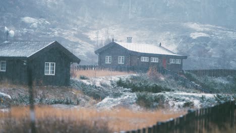 light first snow falls on the withered grass, stones, and roofs of the wooden cabins at the bovertun, norway