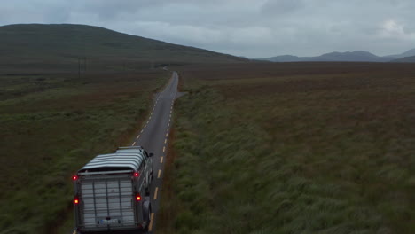 Forwards-fly-behind-vehicle-with-horse-trailer-at-dusk.-Narrow-road-in-countryside-surrounded-by-pastures-and-grasslands.-Ireland