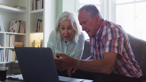Senior couple with laptop using calculator and checking finances while sitting on the couch at home