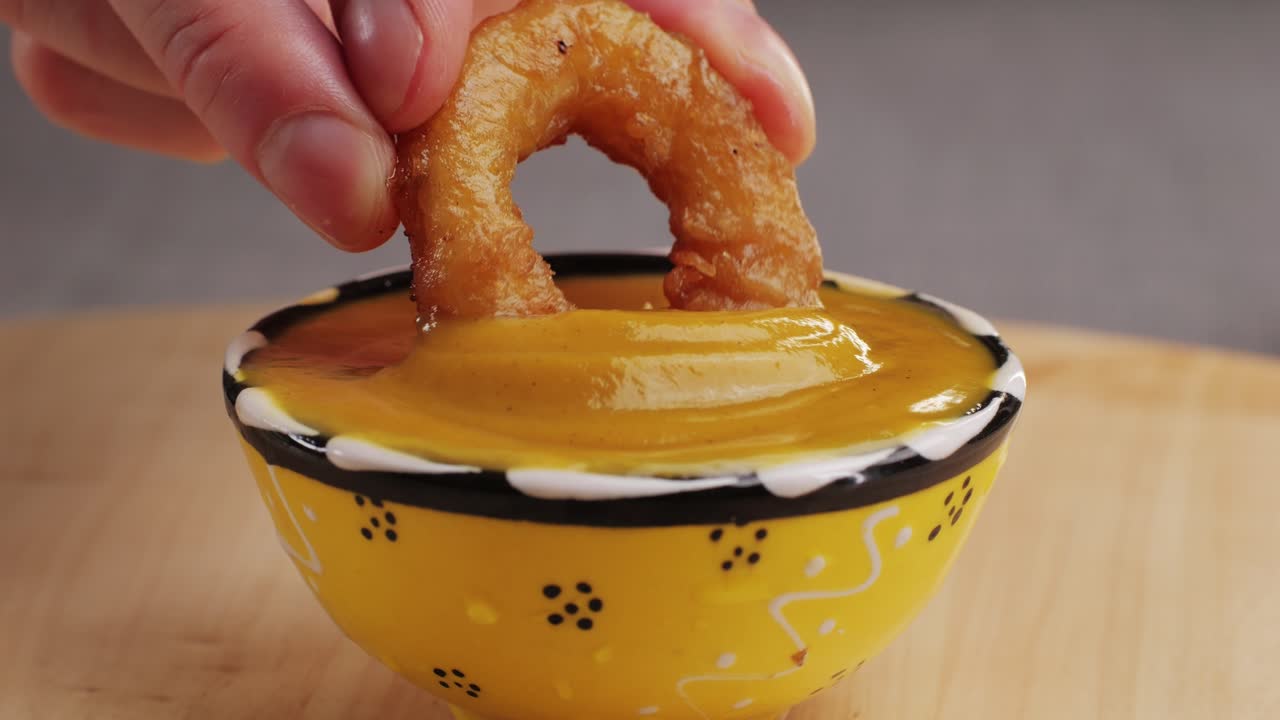 Fried crispy onion rings dipping in chimichuri sauce close-up macro. Roasted onion rings for snacks at bar, cafe. Fast food. Delivery. Beer snacks