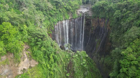 surreal waterfall tumpak sewu falls into deep jungle grotto, java idn