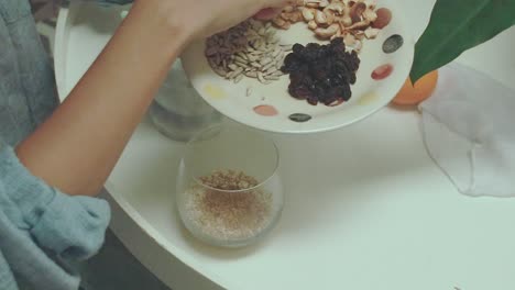 overhead view of adding walnuts, cashew nuts, sunflower seeds and raisins to oats for breakfast showing a candid and healthy morning routine at home