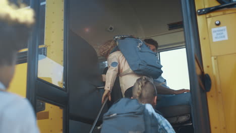 multi ethnic children boarding school bus. focused man driver inspect pupils.