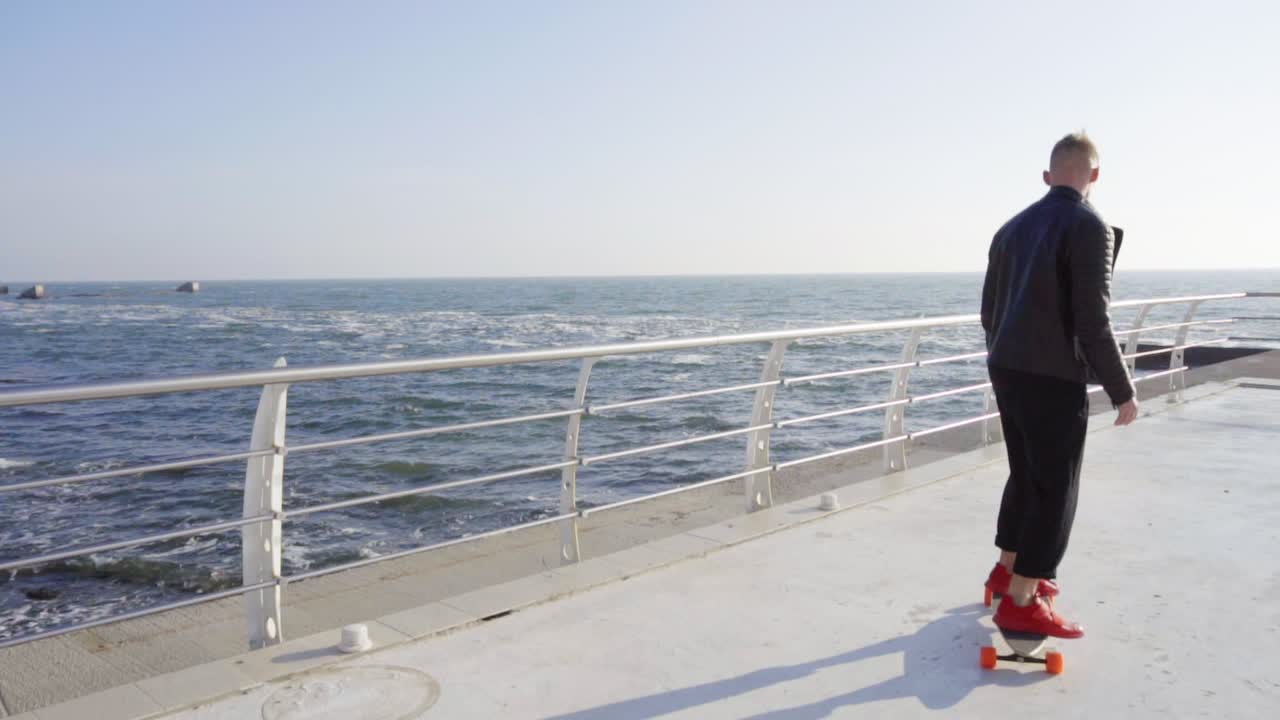 검은색 가죽 재 ⁇ 을 입은 젊은이가 바다에서 스케이트를 타고 있다.