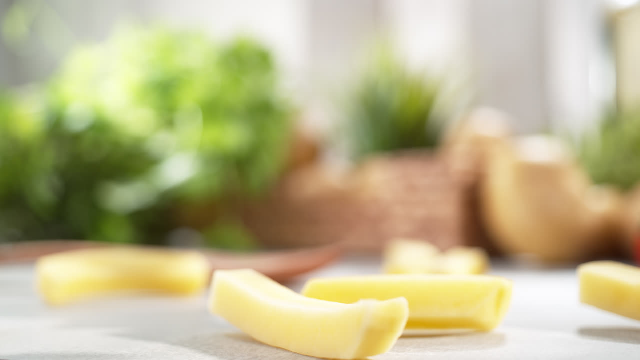 la patata se rompe en papas fritas - un vegetal crudo cae sobre la mesa y se divide en tiras, listo para freír