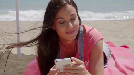 Woman-laying-on-beach-using-cell-phone