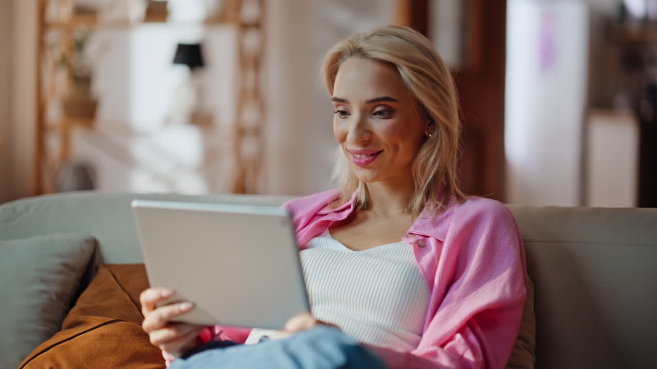 Primo piano di una donna che legge un ebook sul divano di casa. Donna sorridente che ride mentre riceve un'e-mail