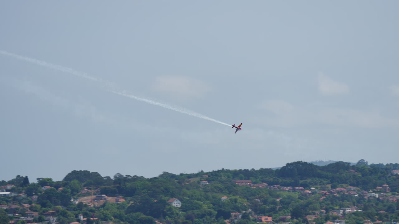 Aerobatic airplane performs maneuver over crowded beach during airshow leaving white smoke trail behind