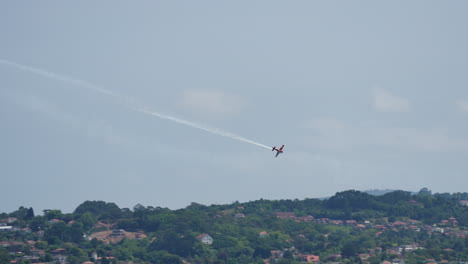 aerobatic airplane performs maneuver over crowded beach during airshow leaving white smoke trail behind