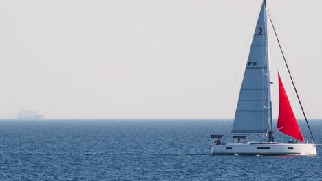 sailboat with red sail moving across ocean