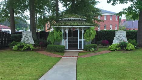 charming white gazebo with moss-covered roof, flanked by ferns and lion-face fountains. wide zoom-in shot