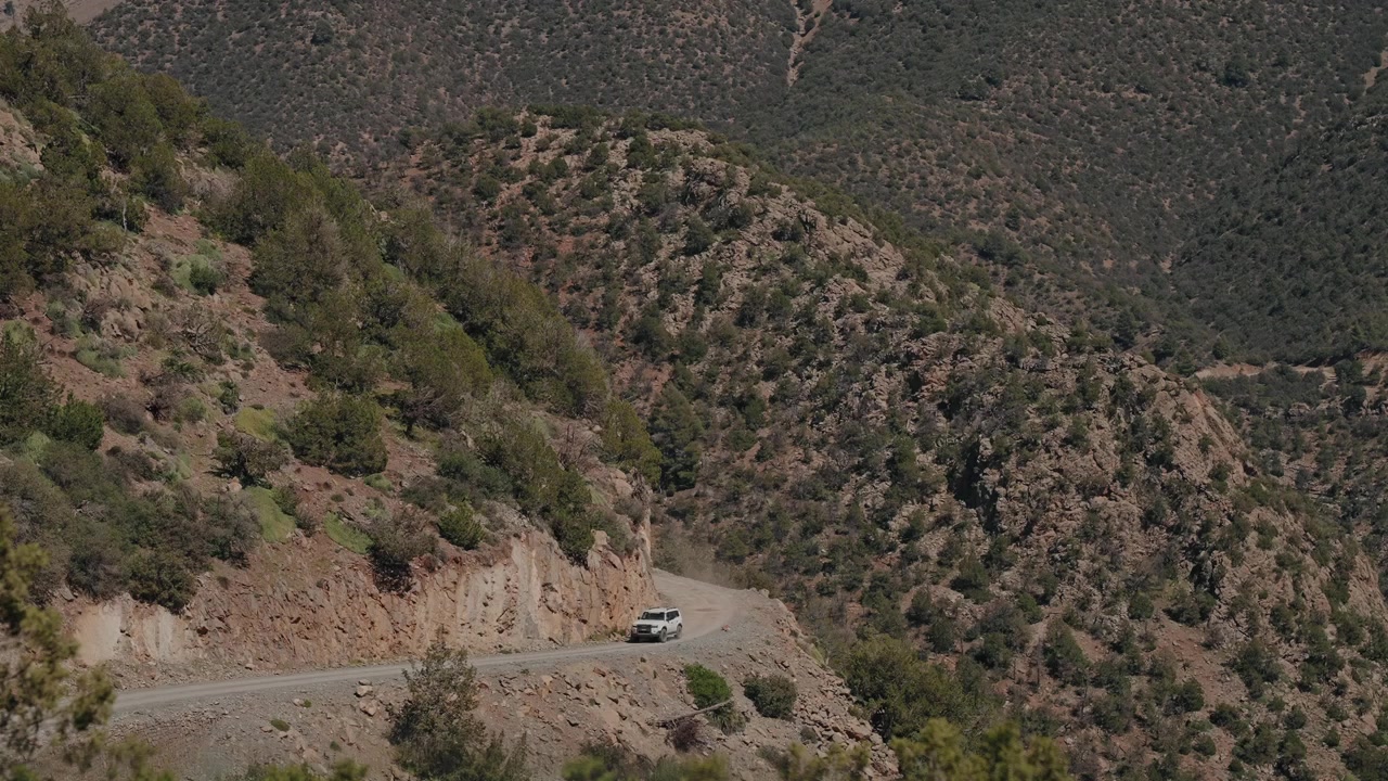 SUV fuoristrada che guida su una stretta strada di montagna a strapiombo su pendii scoscesi coperti di macchia nell'Atlante, Marocco