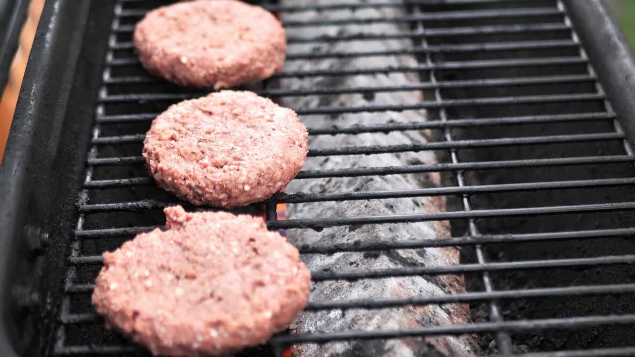 Slow motion 4k footage of a tattooed hand putting alternative meat burgers on a flaming grill on a hot summer day for a barbecue cook out