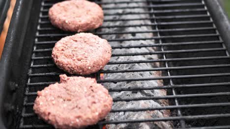 Imágenes-De-4k-En-Cámara-Lenta-De-Una-Mano-Tatuada-Poniendo-Hamburguesas-De-Carne-Alternativas-En-Una-Parrilla-En-Llamas-En-Un-Caluroso-Día-De-Verano-Para-Una-Parrillada