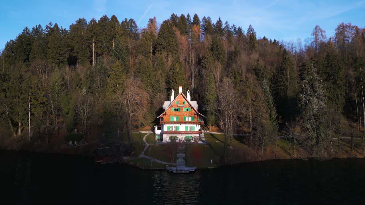 La luce del sole illumina la metà superiore di una baita con vista lago, con il suo riflesso nell'acqua scintillante.