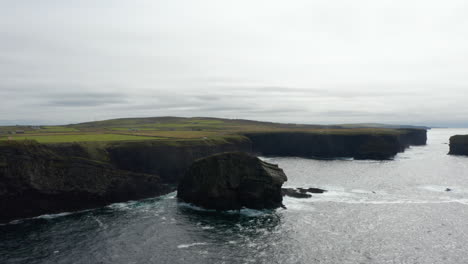 Aerial-panoramic-footage-of-sea-coast-and-rippled-water-surface.-High-vertical-rock-walls-and-pastures-above.-Kilkee-Cliff-Walk,-Ireland