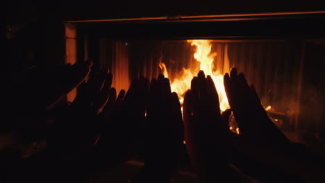 parents with a child warm their hands together by the fire of a fireplace