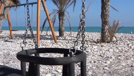 Panoramic-view-on-the-beach-sand,-swings,-palm-trees,-white-sand,-in-the-background-a-beautiful-blue-ocean