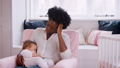 anxious new mother suffering with post natal depression holding sleeping baby girl in nursery at home