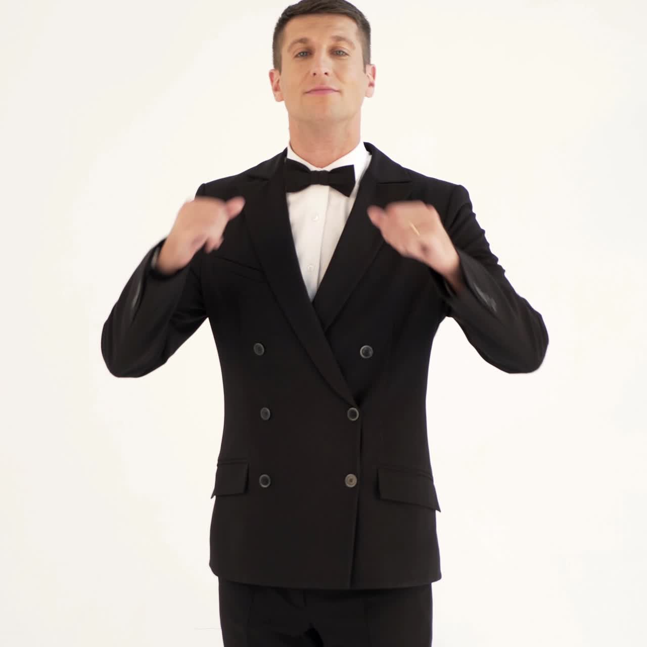 handsome man in a suit with bow-tie is posing in front of a mirror at the exit of the room. Parody of the gentleman on the white background