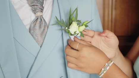 close up of hands pinning a boutonniere on a groom's light blue suit at a wedding
