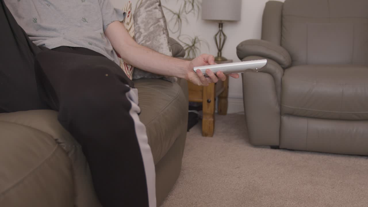 채널을 변경하는 tv 리모콘으로 소파에 게으르게 매달려 있는 남성 손