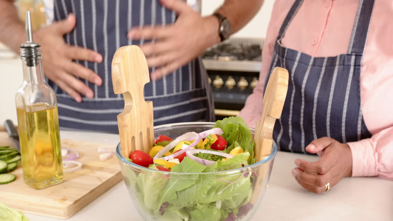 Cooking together in kitchen, senior couple preparing fresh salad with wooden utensils