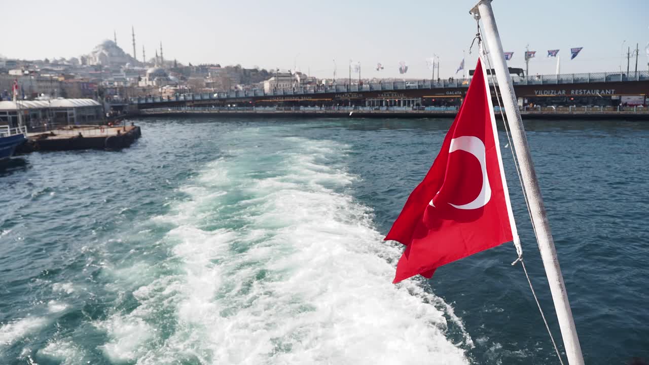 Et rødt tyrkisk flag vajende i vinden på en båd i Bosporusstrædet, med byen Istanbul i baggrunden
