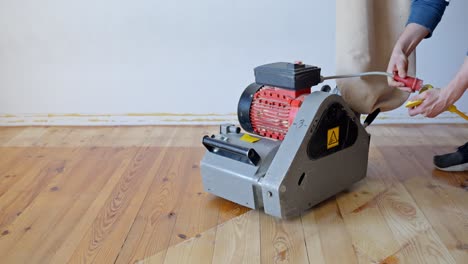 person connects the power plug and activates a wood floor sanding machine on parquet, starting the tool for renovation, visible plug, switch and equipment, static camera, real time, interior scene