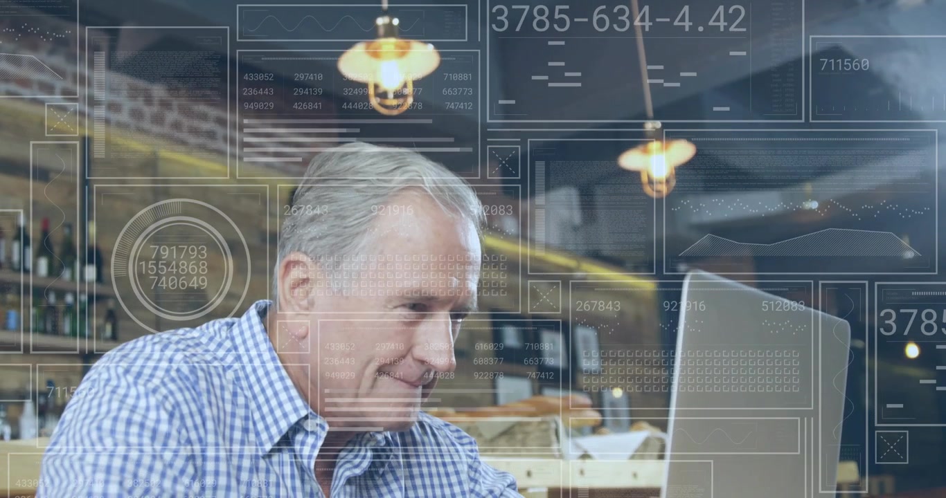 Senior man opening laptop and monitoring finance data overlays while typing beneath pendant lights